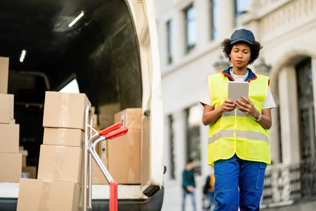 African American Deliverer Using Digital Tablet While Unloading Packages From Van 1 1 1024x683